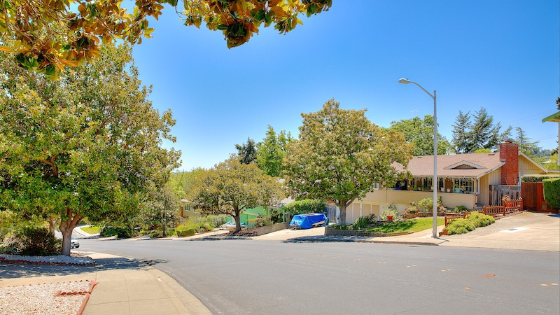 Downhill street view of a two story yellow home with chimney in the Farm Hill Estates area in Redwood City